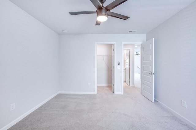 unfurnished bedroom featuring a walk in closet, ceiling fan, a closet, and light colored carpet