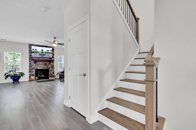 living area featuring ceiling fan, hardwood / wood-style floors, and a stone fireplace