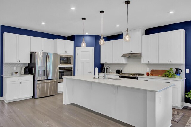 kitchen with pendant lighting, sink, stainless steel stove, light hardwood / wood-style flooring, and a center island with sink