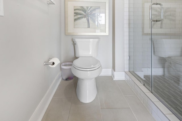 bathroom with toilet, a shower stall, baseboards, and tile patterned floors