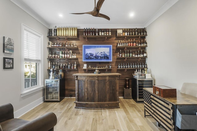 bar with crown molding, a dry bar, a ceiling fan, wood finished floors, and baseboards