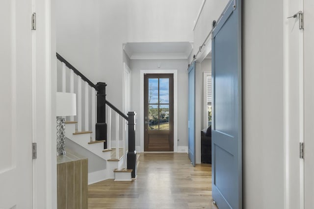 entryway featuring a barn door, wood finished floors, baseboards, stairs, and crown molding