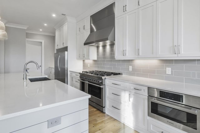 kitchen with a sink, light countertops, appliances with stainless steel finishes, backsplash, and wall chimney exhaust hood