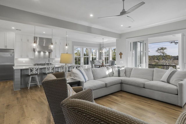 living room with ceiling fan with notable chandelier, recessed lighting, light wood-style flooring, and crown molding