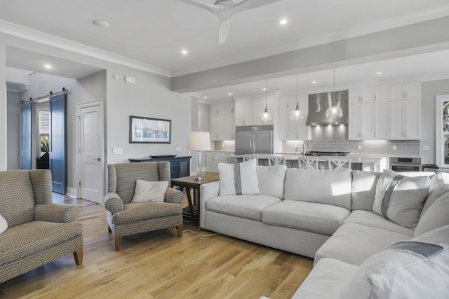 living area with a barn door, recessed lighting, a ceiling fan, light wood finished floors, and crown molding