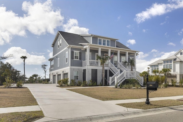 coastal inspired home featuring an attached garage, covered porch, stairs, concrete driveway, and roof with shingles