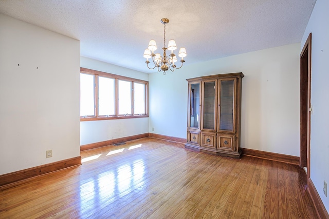 empty room with baseboards, a textured ceiling, a chandelier, and wood finished floors
