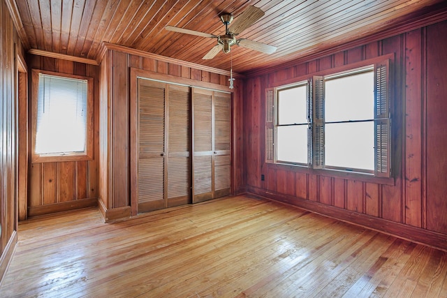 unfurnished bedroom with crown molding, light wood-type flooring, baseboards, a closet, and wooden walls