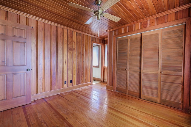 unfurnished bedroom with wooden walls, light wood-style flooring, a ceiling fan, baseboards, and a closet