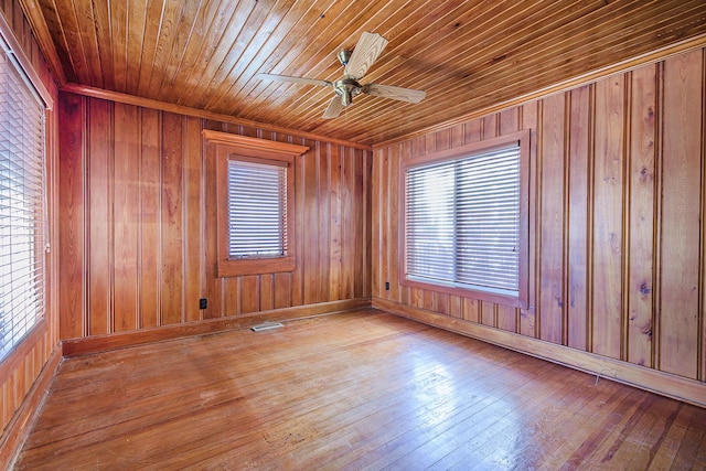unfurnished room featuring wooden walls, ceiling fan, visible vents, and hardwood / wood-style floors