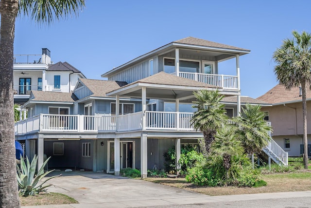 coastal inspired home with driveway, roof with shingles, a carport, stairway, and a balcony