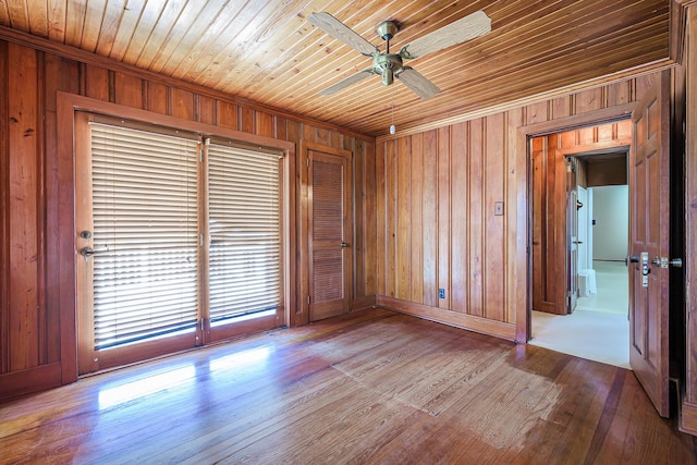 unfurnished room with crown molding, wood walls, a ceiling fan, and wood finished floors