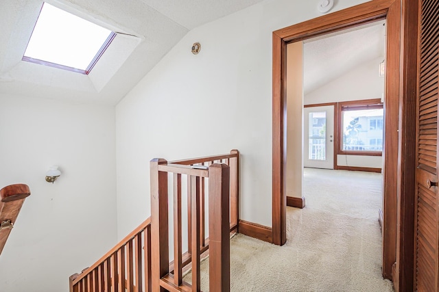 hall with carpet flooring, an upstairs landing, and lofted ceiling with skylight