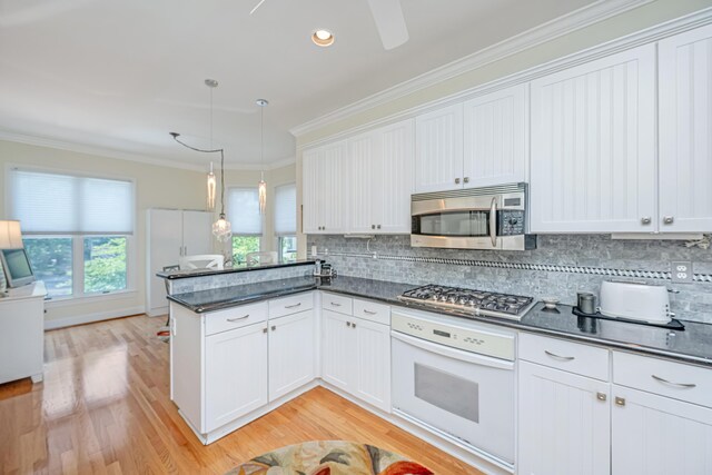 5847 Back Bay Dr, Isle Of Palms, SC 29451 - kitchen featuring appliances with stainless steel finishes, a peninsula, ornamental molding, light wood-style flooring, and tasteful backsplash