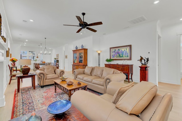 living room with ceiling fan with notable chandelier and light hardwood / wood-style flooring