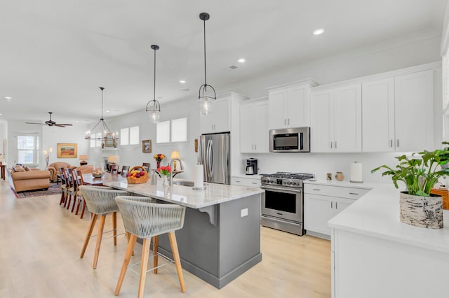 kitchen featuring a breakfast bar, stainless steel appliances, pendant lighting, a center island with sink, and white cabinets