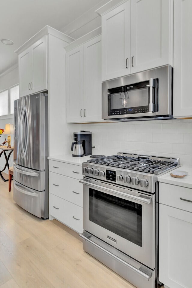 kitchen with backsplash, ornamental molding, stainless steel appliances, light hardwood / wood-style floors, and white cabinetry