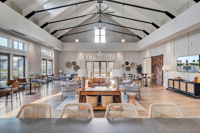 living room featuring a barn door, light hardwood / wood-style floors, high vaulted ceiling, and ceiling fan