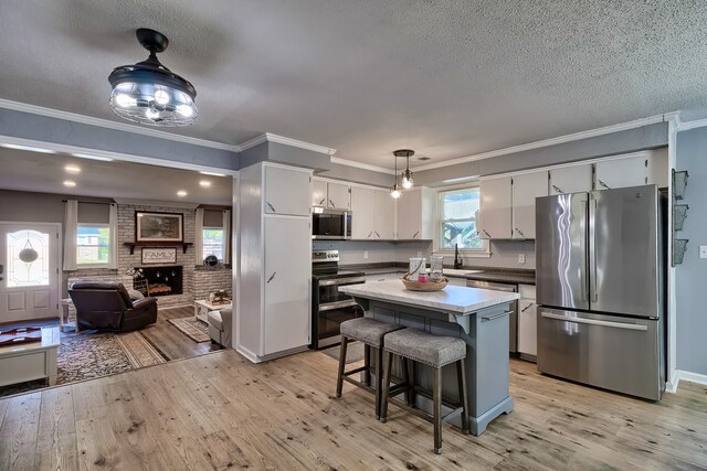 kitchen with stainless steel appliances, a center island, white cabinetry, light hardwood / wood-style flooring, and decorative light fixtures