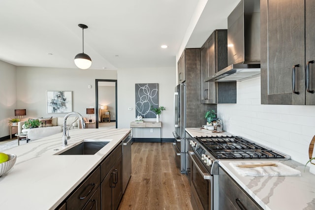 kitchen with stainless steel appliances, a sink, wall chimney range hood, wood finished floors, and dark brown cabinetry