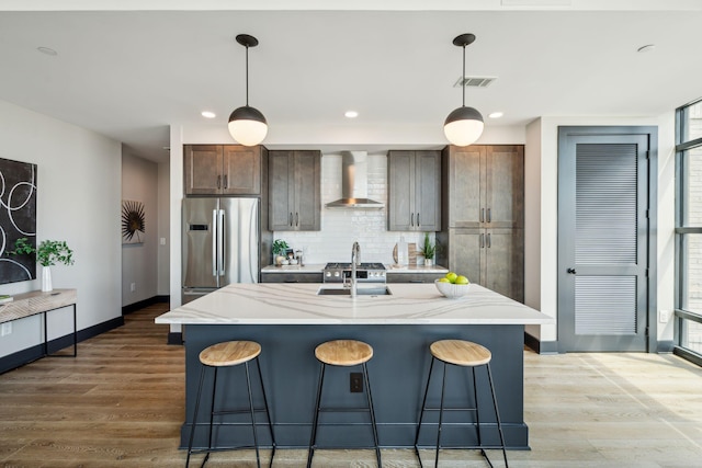 kitchen featuring wall chimney exhaust hood, freestanding refrigerator, baseboards, light wood-style flooring, and recessed lighting