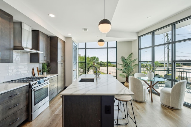 kitchen with stainless steel gas range oven, wall chimney range hood, a sink, backsplash, and a breakfast bar