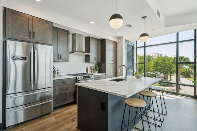 kitchen featuring stainless steel fridge, wall chimney exhaust hood, a sink, backsplash, and wood finished floors