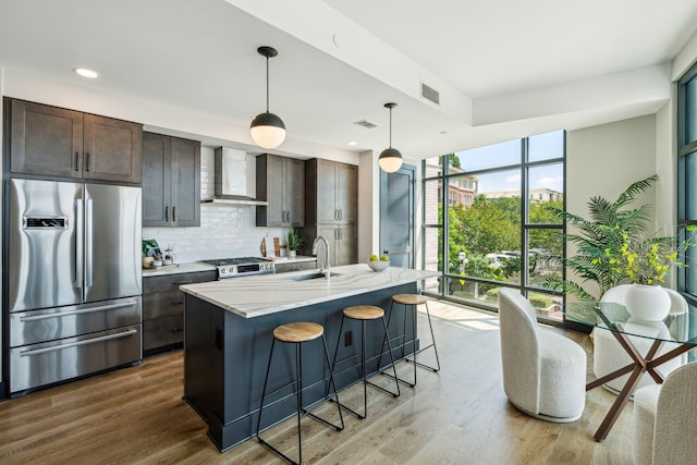 kitchen with freestanding refrigerator, wall chimney range hood, a sink, backsplash, and dark brown cabinetry