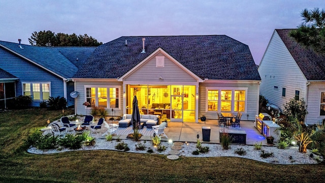 back house at dusk with a patio area and a lawn