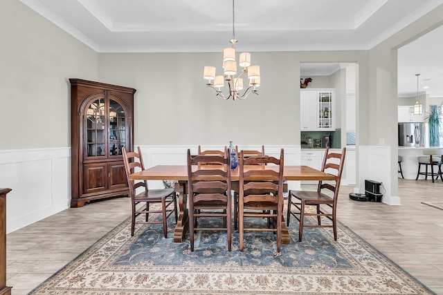 dining room featuring an inviting chandelier, ornamental molding, a tray ceiling, and light wood-type flooring