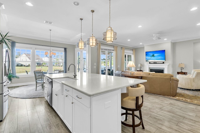 kitchen with pendant lighting, light wood-type flooring, an island with sink, and white cabinets