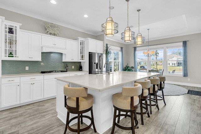 kitchen featuring white cabinets, stainless steel fridge with ice dispenser, hanging light fixtures, and a center island with sink