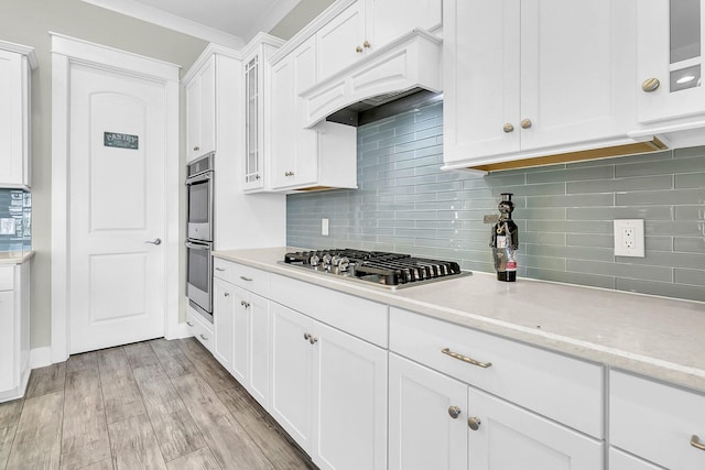 kitchen with appliances with stainless steel finishes, white cabinetry, light stone countertops, decorative backsplash, and light wood-type flooring