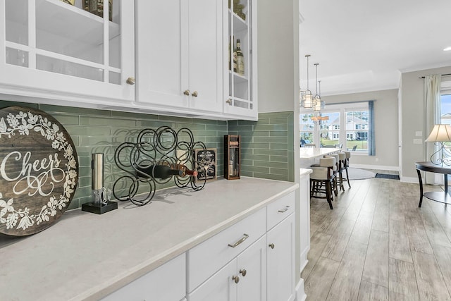 bar with hanging light fixtures, white cabinetry, backsplash, and light hardwood / wood-style flooring