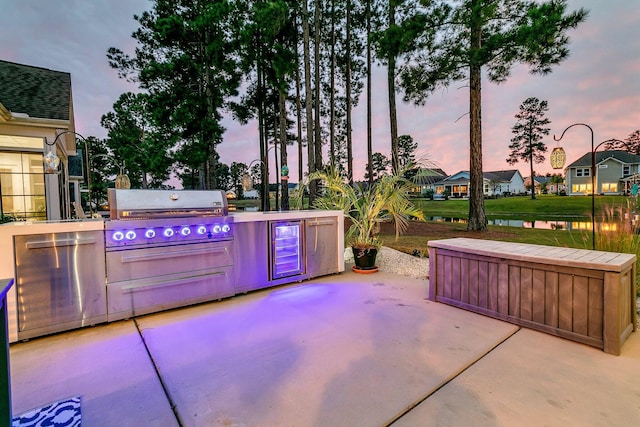 patio terrace at dusk with area for grilling, a water view, and exterior kitchen