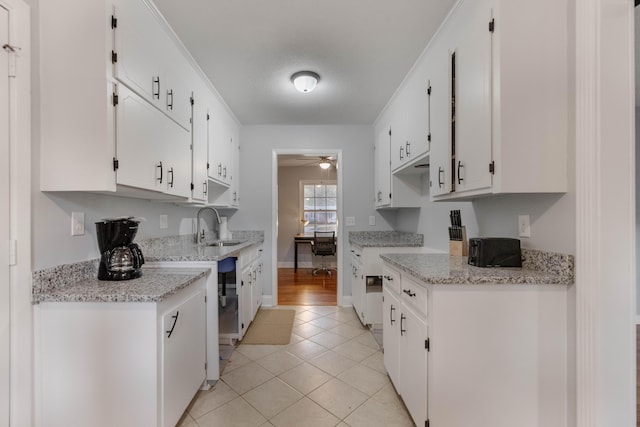 kitchen with light stone countertops, light tile patterned floors, white cabinetry, and sink