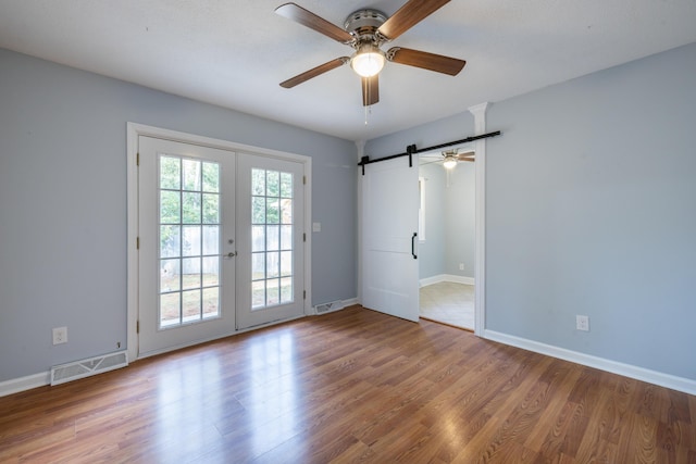 empty room with a barn door, ceiling fan, hardwood / wood-style floors, and french doors