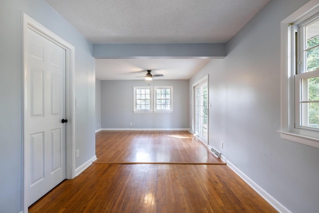 empty room featuring ceiling fan, wood-type flooring, a textured ceiling, and a wealth of natural light