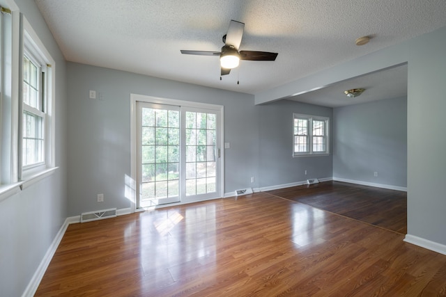 spare room with a textured ceiling, dark hardwood / wood-style floors, ceiling fan, and a healthy amount of sunlight