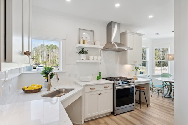 kitchen with sink, white cabinetry, wall chimney exhaust hood, stainless steel gas stove, and light stone countertops