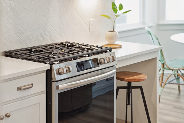 kitchen with stainless steel range, light hardwood / wood-style floors, white cabinetry, and decorative backsplash