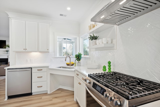 kitchen with ventilation hood, white cabinets, light hardwood / wood-style flooring, backsplash, and appliances with stainless steel finishes