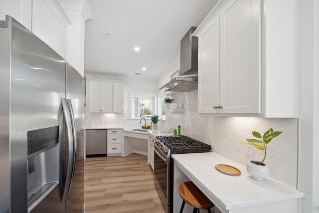 kitchen with light hardwood / wood-style floors, white cabinets, wall chimney exhaust hood, decorative backsplash, and appliances with stainless steel finishes