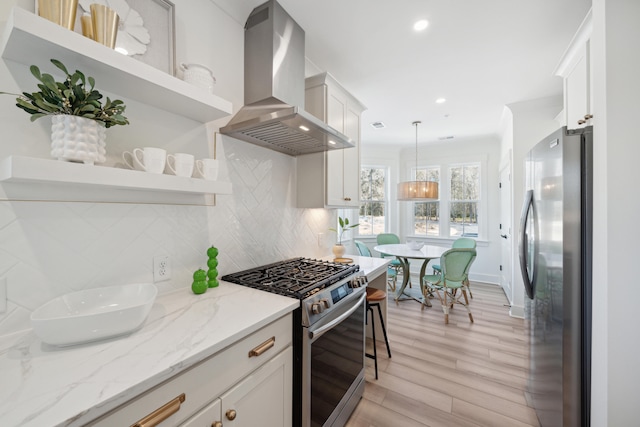 kitchen featuring hanging light fixtures, backsplash, wall chimney range hood, stainless steel appliances, and light hardwood / wood-style floors