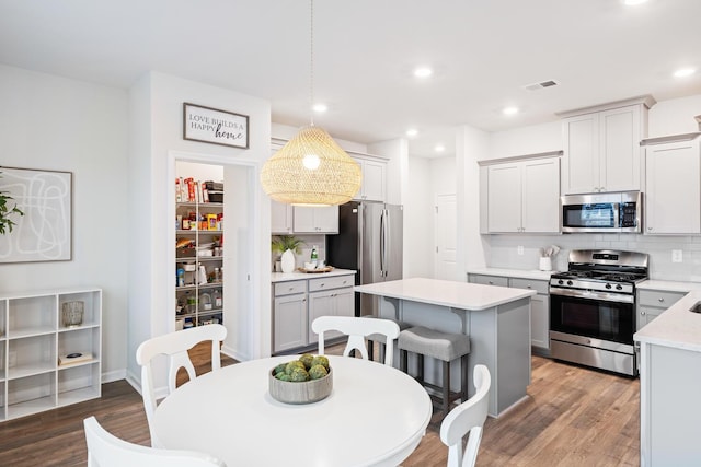 kitchen with appliances with stainless steel finishes, hanging light fixtures, backsplash, hardwood / wood-style floors, and a center island