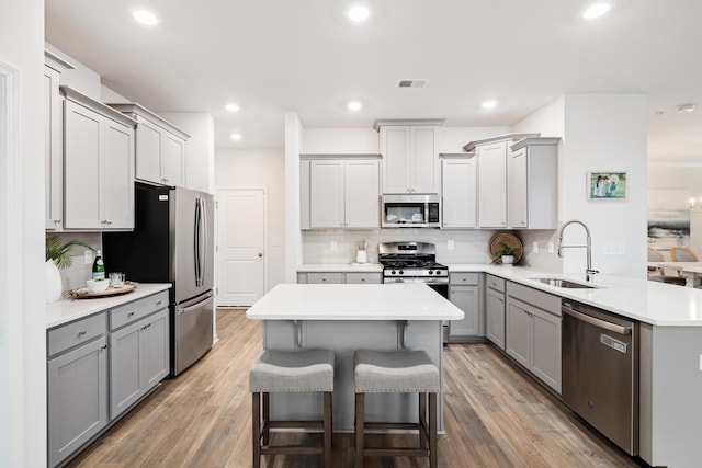 kitchen with gray cabinetry, sink, a breakfast bar, and appliances with stainless steel finishes