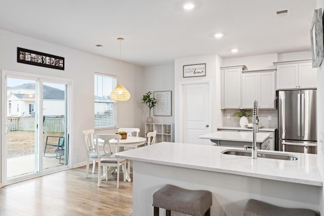 kitchen featuring pendant lighting, stainless steel fridge, light stone counters, tasteful backsplash, and light hardwood / wood-style floors