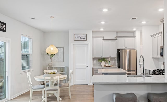 kitchen with appliances with stainless steel finishes, pendant lighting, backsplash, light stone counters, and light wood-type flooring