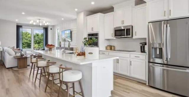 kitchen with stainless steel appliances, light wood-type flooring, a kitchen island with sink, light countertops, and recessed lighting