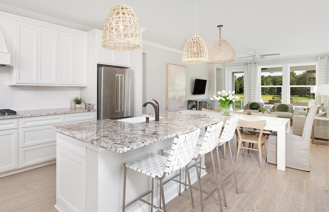 kitchen with appliances with stainless steel finishes, ceiling fan, a kitchen island with sink, decorative light fixtures, and white cabinetry